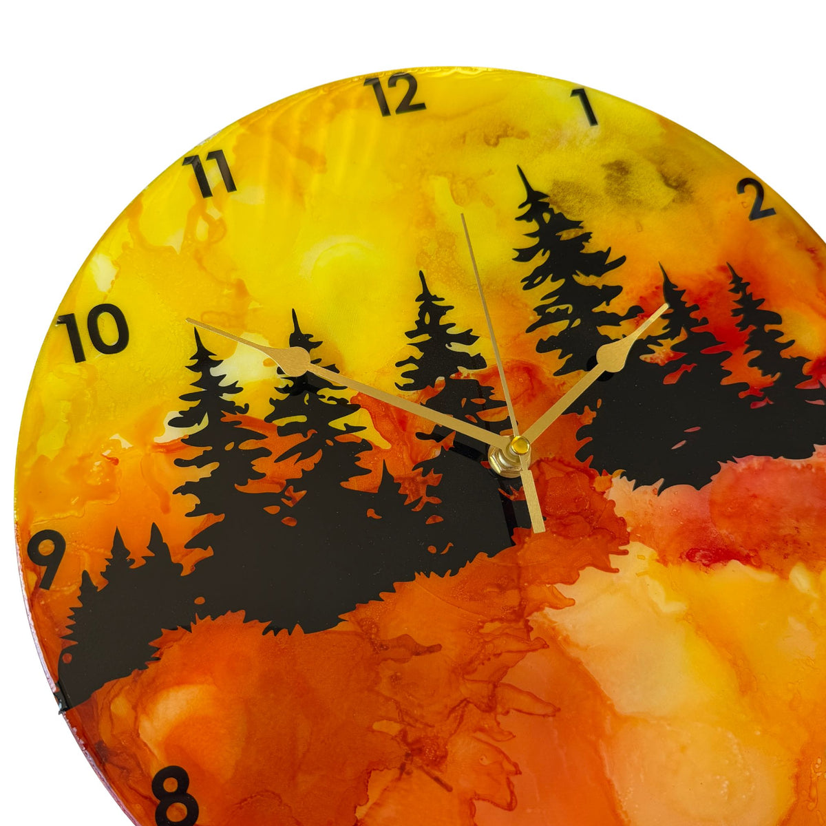 A round wall clock with a vibrant alcohol ink landscape design featuring black pine tree silhouettes over a gradient of yellow, orange, and red, with black Arabic numerals and gold hands.