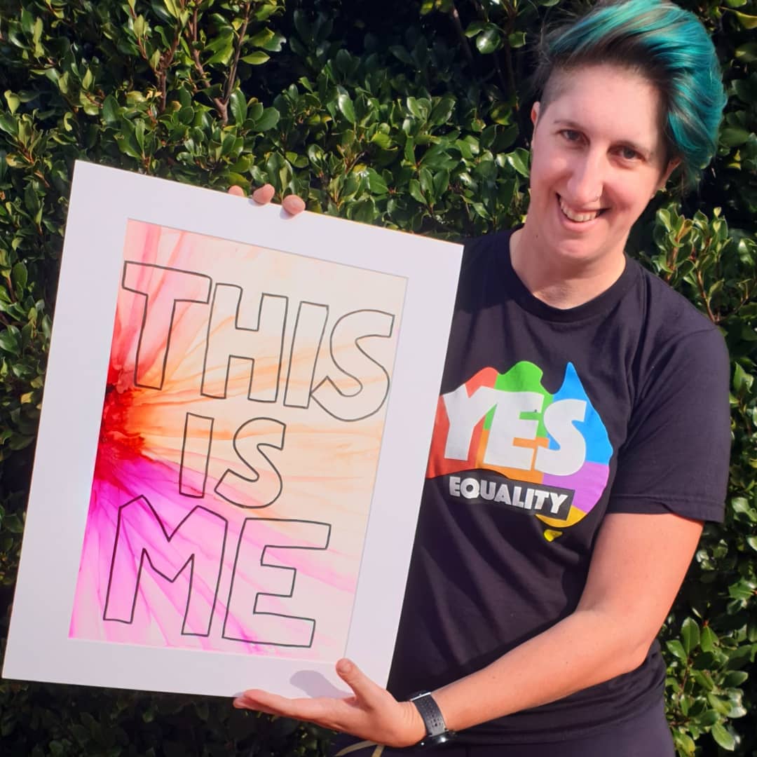 Vanessa is holding artwork that says "This Is Me", and is smiling at the camera.