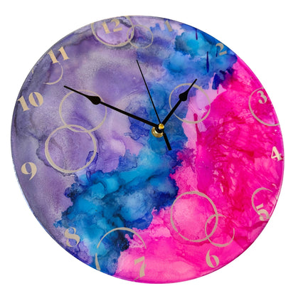 A round wall clock with a vibrant design in purple, blue, and pink, featuring silver numerals and black hands.