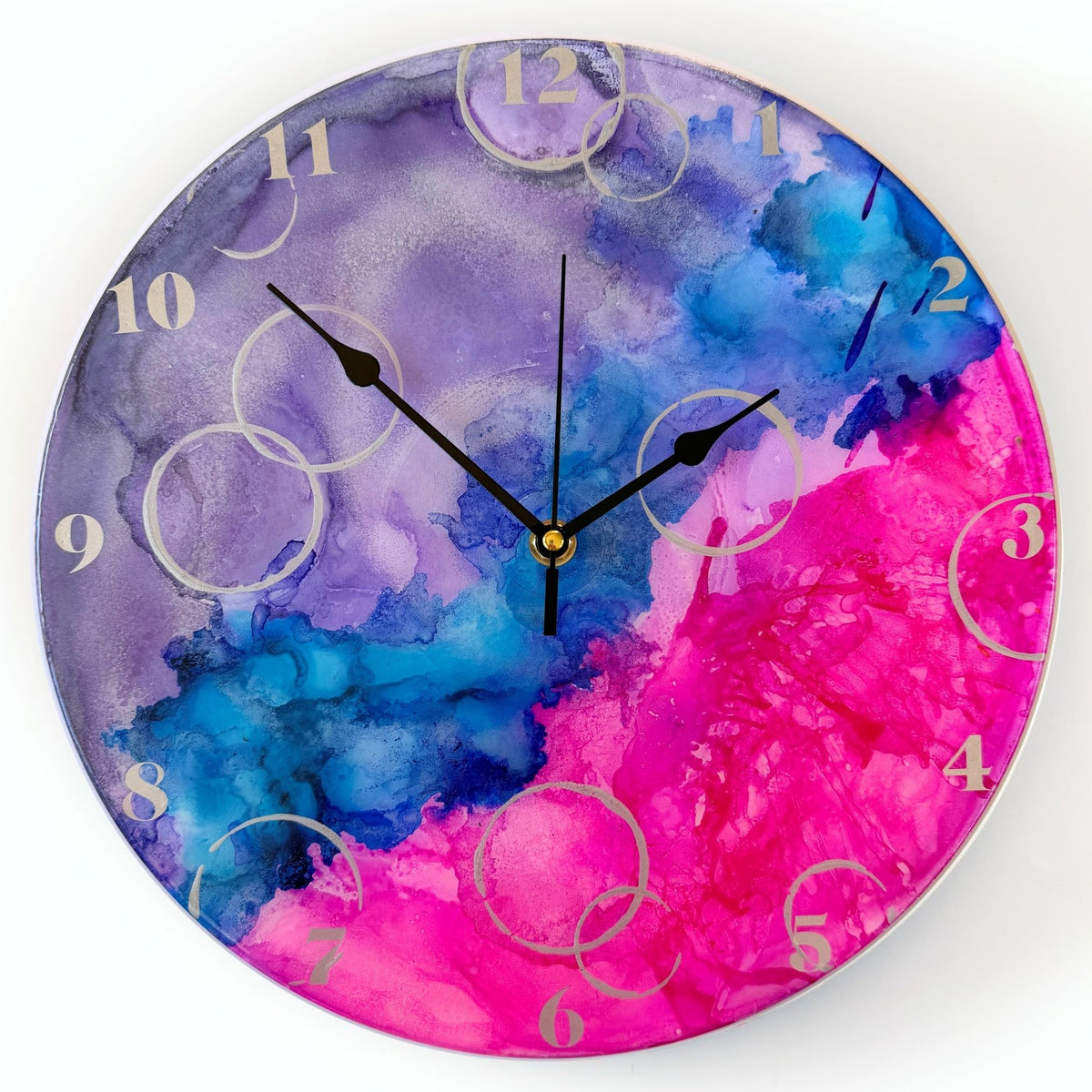 Round wall clock with a vibrant design in purple, blue, and pink, featuring black hands and light silver Arabic numerals.