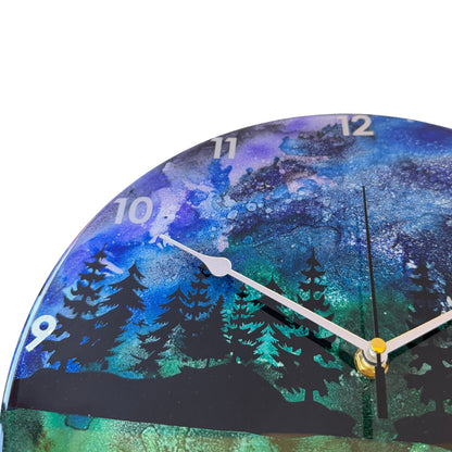 Round wall clock with a scenic forest landscape print in blue, green, and black, featuring silver hands and white Arabic numerals.