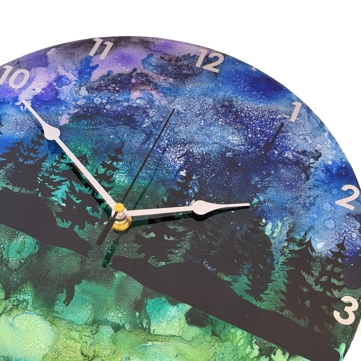 Round wall clock with a scenic forest landscape print in blue, green, and black, featuring silver hands and white Arabic numerals.