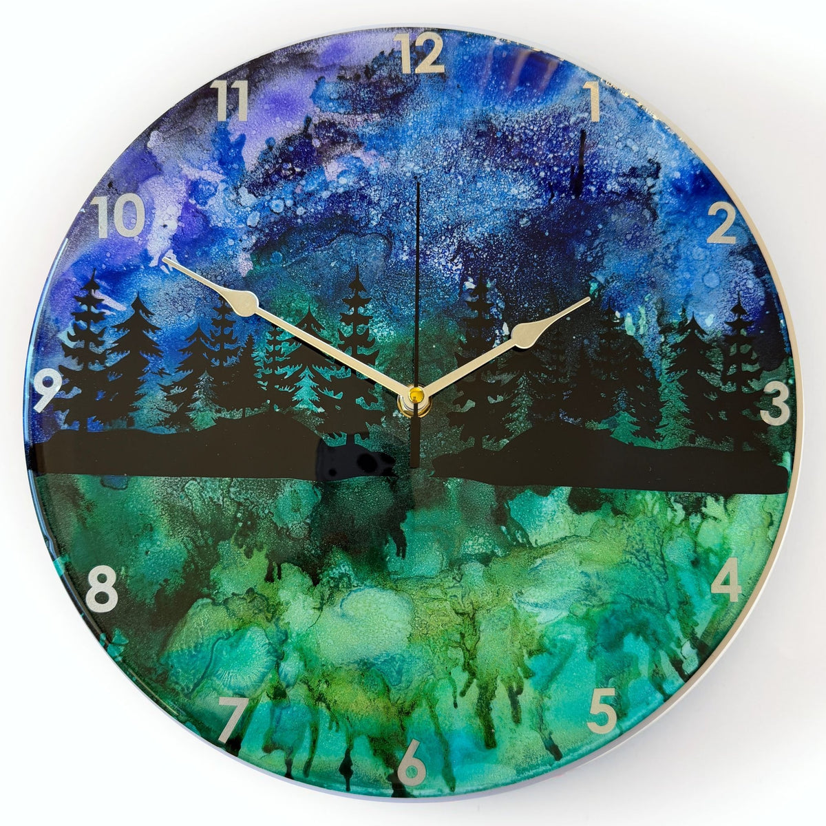 Round wall clock with a scenic forest landscape print in blue, green, and black, featuring silver hands and white Arabic numerals.