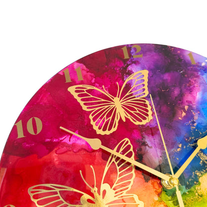 Round wall clock with a vibrant rainbow design and gold butterfly illustrations, with gold arabic numerals and gold hands.