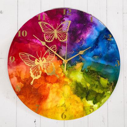 Round wall clock with a vibrant rainbow design and gold butterfly illustrations, with gold arabic numerals and gold hands.