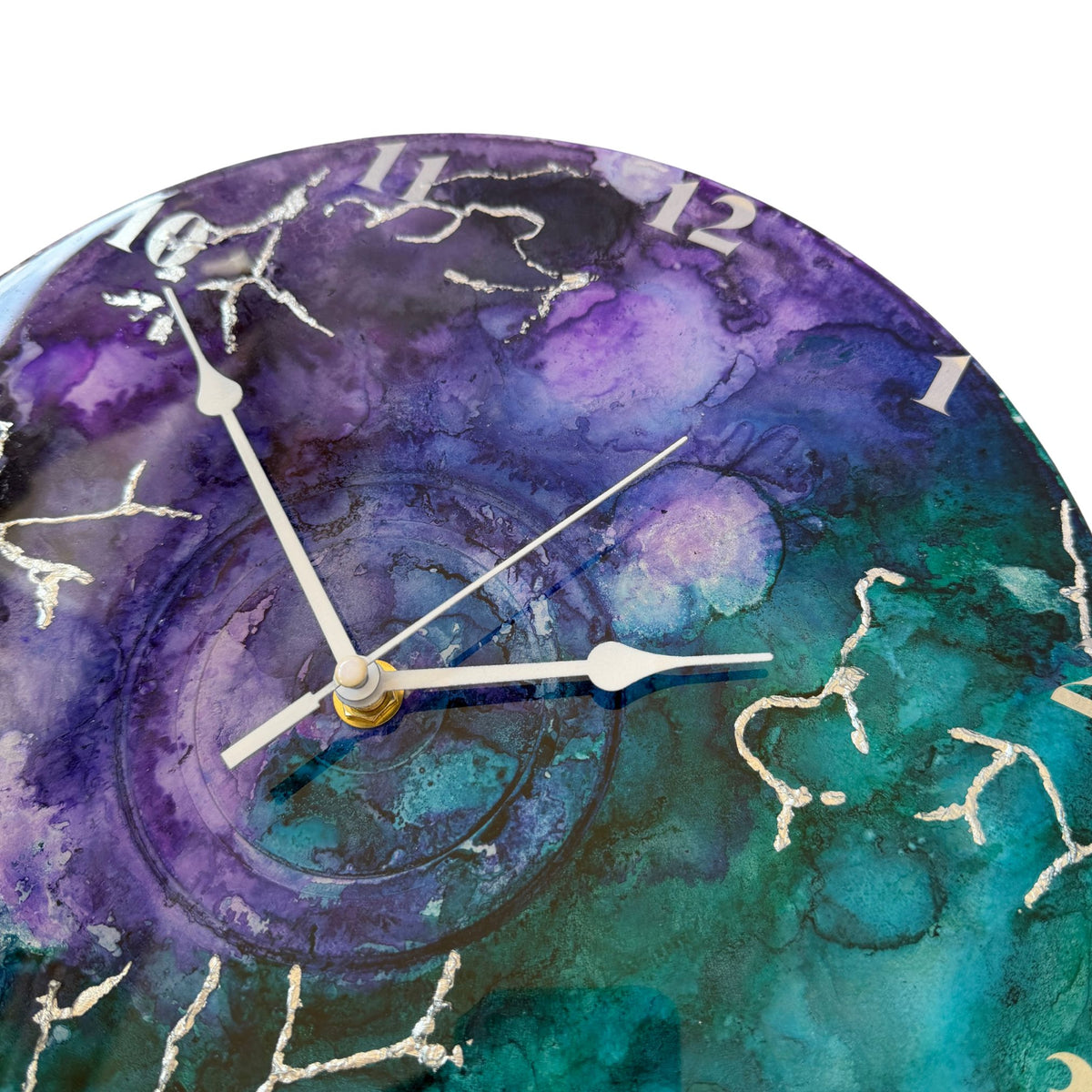 Round wall clock with a watercolour-style marbled face in purple, teal, and blue, with silver clock hands and silver Arabic numerals.