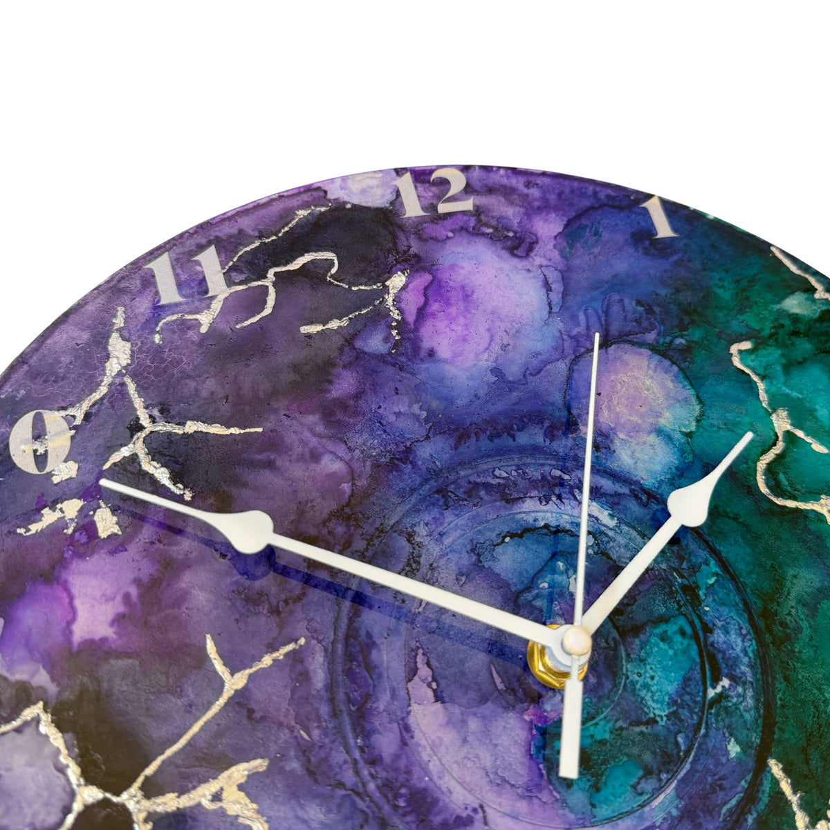 Round wall clock with a watercolour-style marbled face in purple, teal, and blue, with silver clock hands and silver Arabic numerals.