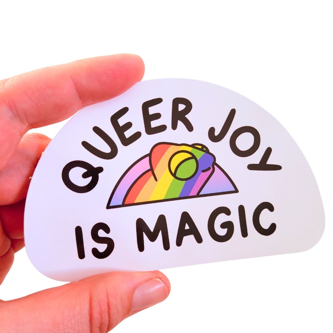 Sticker with 'Queer Joy is Magic' text and rainbow chameleon design held by a hand on a white background